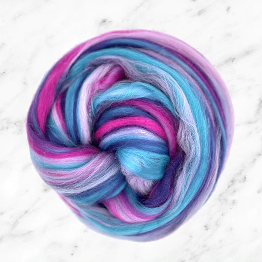 A brightly colored teal, magenta, and purple ball of wool fiber resting on a marble surface